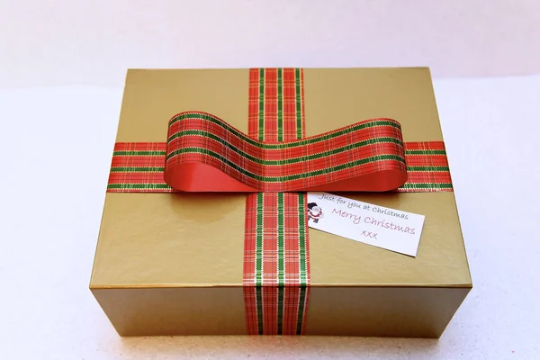 Kişiselleştirilmiş noel hediyesi, üzerinde tartan kurdele olan altın bir kutuda.