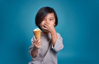 Mutlu gülümseyen Asyalı çocuk burnunu tutuyor ve lezzetli bir dondurmayla. Stüdyodaki boş alan, renkli mavi arka planda izole edilmiş. Okul için eğitim kavramı.