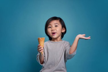 Mutlu gülümseyen Asyalı küçük çocuk elinde lezzetli bir dondurma tutuyor. Stüdyodaki boş alan, renkli mavi arka planda izole edilmiş. Okul için eğitim konsepti. Okul için eğitim kavramı.