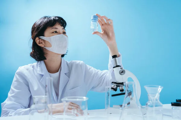 研究室のコートのスマート若いアジアの女性科学者医療面マスク 実験器具の検査 スタジオでの空のスペースは カラフルな青の背景に隔離されたショット 医学的概念 — ストック写真