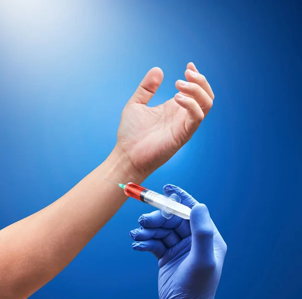 Doctor hand with medical needle syringe drug for injection on another hand. Deep blue background. Medical concept for health care, research, and science.