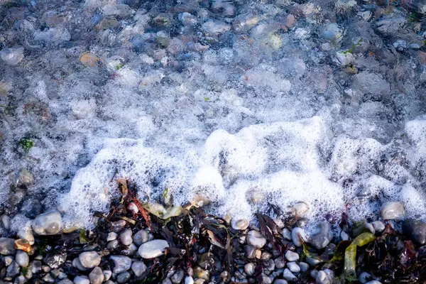 Fala z pianką na żwirowej plaży. — Zdjęcie stockowe