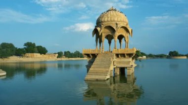 Su kütlesinin ortasındaki sarı taştan yapılar, Jaisalmer şehrindeki Gadisar Gölü, su korunması için yapay olarak inşa edilmiştir. Jaisalmer, Rajasthan, Hindistan 'da vuruldu. Mavi gökyüzü arkaplanı.