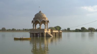 Su kütlesinin ortasındaki sarı taştan yapılar, Jaisalmer şehrindeki Gadisar Gölü, su korunması için yapay olarak inşa edilmiştir. Jaisalmer, Rajasthan, Hindistan 'da vuruldu. Mavi gökyüzü arkaplanı.