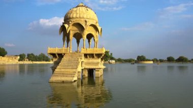 Su kütlesinin ortasındaki sarı taştan yapılar, Jaisalmer şehrindeki Gadisar Gölü, su korunması için yapay olarak inşa edilmiştir. Jaisalmer, Rajasthan, Hindistan 'da vuruldu. Mavi gökyüzü arkaplanı.