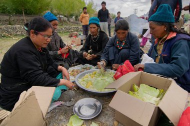 Mulbekh, Ladakh, Hindistan - 2 Eylül 2014: Geleneksel elbiseli Ladakhi kabile kadınları arka planda Himalaya dağları, dini festival için sebze kesiyor.