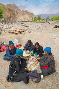 Mulbekh, Ladakh, Hindistan - 2 Eylül 2014: Geleneksel elbiseli Ladakhi kabile kadınları arka planda Himalaya dağları, dini festival için sebze kesiyor.