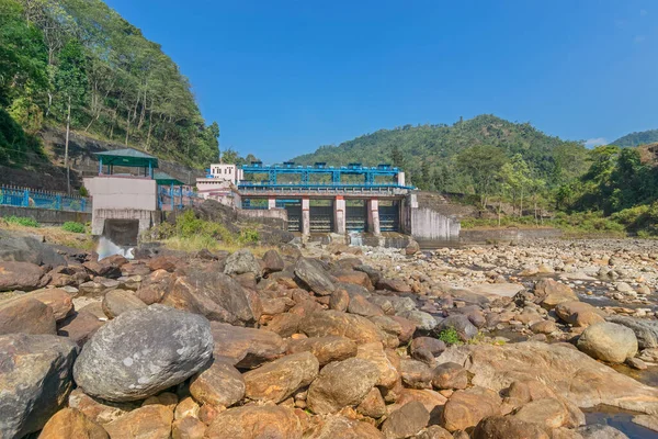 DOOARS, Batı BENGAL, INDIA - 6 ARALIK 2017 Joldhaka nehir projesi - Joldhaka nehri kıyısındaki hidroelektrik santrali. Önplanda nehir kıyısının taşları ve arkada mavi gökyüzü.