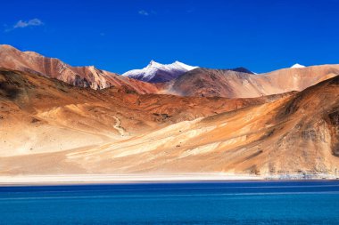 Dağlar ve Pangong (Göl). Ladakh 'ta büyük bir göl olup, arka planda kar zirveleri ve mavi gökyüzü ile Hindistan' dan Tibet 'e kadar uzanır. Leh, Ladakh, Jammu ve Kashmir, Hindistan