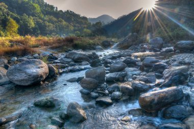 Güzel Reshi Nehri 'nin suları şafak vakti kayaların üzerinde akıyor, Sikkim, Hindistan - arka planda güneş ışınları suya düşüyor ve muhteşem bir manzara yaratıyor 
