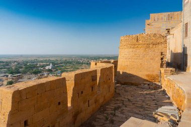 Jaisalmer, Rajasthan, Hindistan - 13 Ekim 2019: Jaisalmer Kalesi veya Altın Kale 'nin büyük duvarları, sarı kumtaşından yapılmış, sabah ışığında şehrin bir kısmı çerçevede. UNESCO dünya mirası sahası.