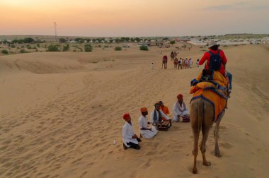 Thar Çölü, Rajassthan, Hindistan - 15 Ekim 2019: Thar Çölü 'nün kum tepelerinde deve sürüşü sırasında yerel halkla etkileşime geçen bir kadın turist. Deve binme turistler arasında favoridir..