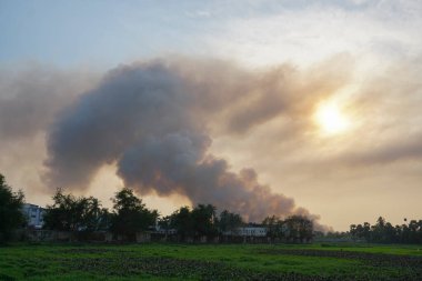 Ufuktaki fabrikalardan duman çıkıyor, hava kirliliği bulutlar gibi yayılıyor ve batan güneşi kaplıyor. Batı Bengal, Hindistan kırsal köyünde vuruldu. Kirlilik dünya çapında bir sorundur..