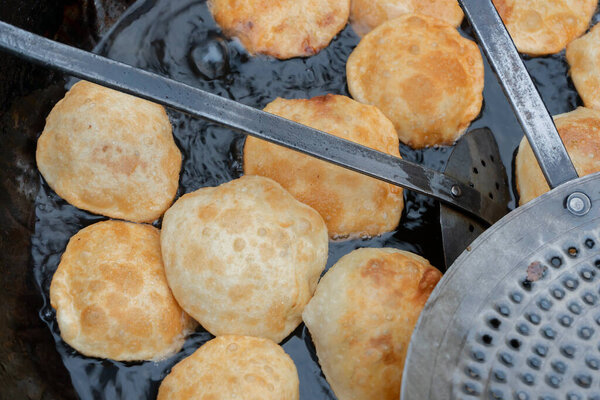 Many Kochuris are being fried in a frying pan. Kochuri, kachori of kachauri is a spicy snack, fried dumpling and a very popular street food in India.