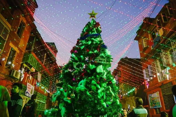 KOLKATA, WEST BENGAL, INDIA - DECEMBER 24TH 2017 : A big christmas tree is illuminated with lights at Bow Barracks - a famous Anglo-Indian street of Kolkata, at night. Decorative lights overhead.