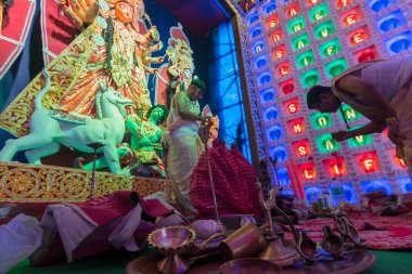 Howrah, Batı Bengal, Hindistan - 5 Ekim 2019: Durga Puja sırasında Durga Puja pandalında tanrıça Durga 'ya tapınmak için kutsal çömlekleri hazırlayan genç Hindu Bengalli rahipler. Renkli ışığın altında çekilen.