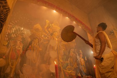 KOLKATA, INDIA - SEPTEMBER 27, 2017: Saptami Puja - Tanrıça Durga 'ya tapan genç Hindu rahip kutsal duman altında, Durga Puja festivali ritüeli. Gece çekilen renkli ışığın altında.