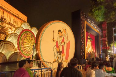 KOLKATA, INDIA - SEPTEMBER 28, 2017: Hizmetçi kulak karıştırıcı ile bir bengali seçiyor - boya, dışarıda süslenmiş Durga Puja pandalı - gece renkli ışıklarda çekiliyor.