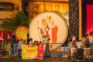KOLKATA, INDIA - SEPTEMBER 28, 2017: Hizmetçi kulak karıştırıcı ile bir bengali seçiyor - boya, dışarıda süslenmiş Durga Puja pandalı - gece renkli ışıklarda çekiliyor.