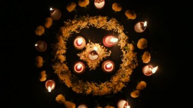 Rangoli çiçeklerinin daire şeklinde üst görüntüsü ve içine konmuş mumlar veya diyalar, geceleri Deepawali ışıkları. Koyu arkaplan Stok görüntüleri.