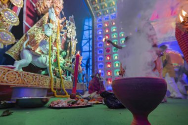 Howrah, Batı Bengal, Hindistan - 5 Ekim 2019: Durga Puja sırasında Aarti Hindu ayini sırasında dumanla kaplı tanrıça Durga 'ya tapan Hindu Bengalli rahipler. Renkli ışığın altında çekilen.