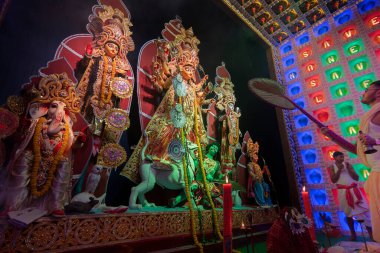 Howrah, Batı Bengal, Hindistan - 5 Ekim 2019: Genç Hindu Bengali purohit el vantilatörüyle tanrıça Durga 'ya tapıyor, Durga aarti gece puja pandalının içinde renkli ışık altında çekim yapıyor.
