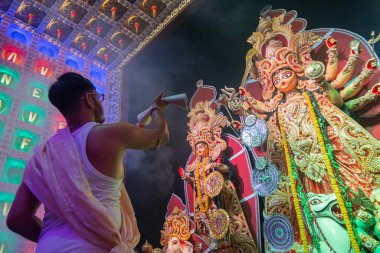 Howrah, Batı Bengal, Hindistan 5 Ekim 2019 Hindu Bengali purohit Tanrıça Durga 'ya Durga Puja sırasında kutsal dumanın altında geleneksel Hint kadın elbisesi sunuyor. Alttan çekilmiş, renkli ışık..