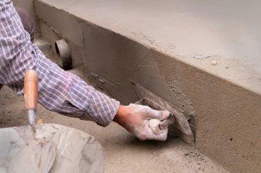 Düz mala ve çimento kullanarak zeminin alçılı yan duvarını elle döşeyen Hint işçiliği. Stok resmi..