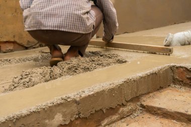 Hintli inşaat işçisi ahşap dengeleyiciyi elle kullanarak beton zemini düzleştiriyor..