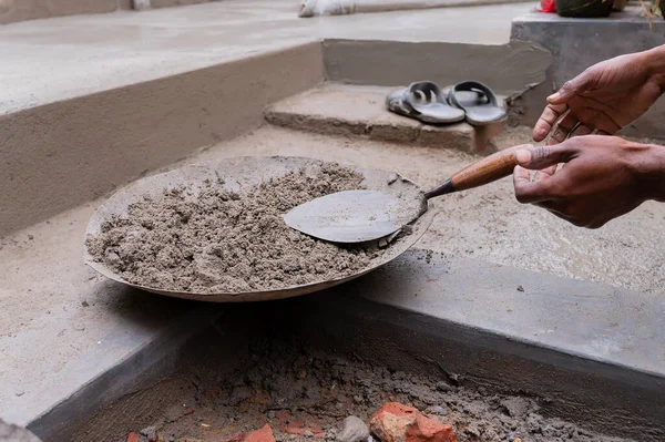 Indian labour preparing cement for plastering manually on bucket using trowel with bare hands. Stcok image.