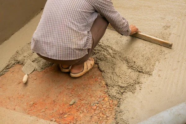 Indian construction worker levelling a cemented floor using wooden tool manually, Stock image.