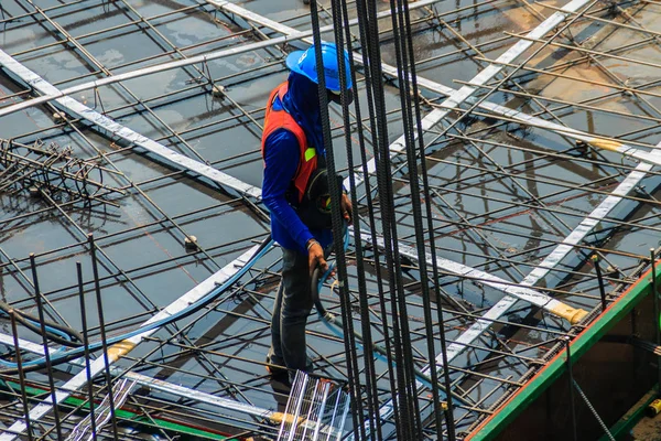 Unidentified worker used the high pressure machine to clean floor slab reinforcement bar with post tension cable tendon on steel form work at the construction site before concreting.