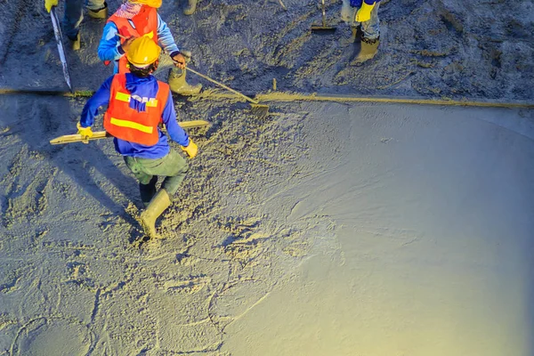 Mason worker leveling concrete with trowels, mason hands spreading poured concrete. Concreting workers are leveling poured liquid concrete on a steel reinforcement to form strong floor slab.