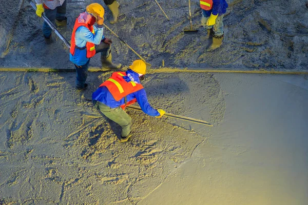 Mason worker leveling concrete with trowels, mason hands spreading poured concrete. Concreting workers are leveling poured liquid concrete on a steel reinforcement to form strong floor slab.