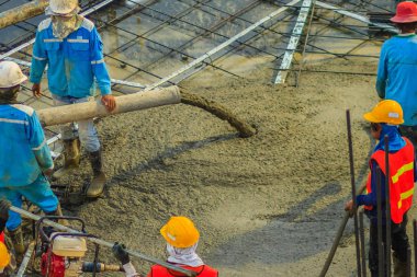 İnşaat işçileri beton sonrası gerginlik döşeme çalışmalarında yağıyor. Mason işçiler iş inşaat sahasında betonlama sırasında hortum beton pompası ya da diğer adıyla fil hortumu taşıyan