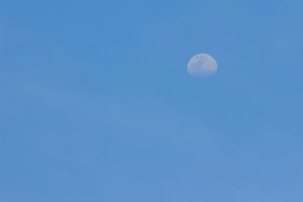 Moon on clear blue sky during the day. Half moon on the blue sky just before sunset.