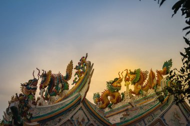 Güzel büyük yüz buruşturma ejderha Çin tapınaklarda dekoratif kiremit çatı üzerinde sürünerek. Geleneksel Çince Tapınağı ile ejderha heykeli mavi gökyüzü arka plan üzerinde renkli çatı detay.