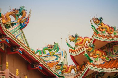 Güzel büyük yüz buruşturma ejderha Çin tapınaklarda dekoratif kiremit çatı üzerinde sürünerek. Geleneksel Çince Tapınağı ile ejderha heykeli mavi gökyüzü arka plan üzerinde renkli çatı detay.