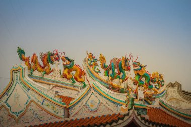 Güzel büyük yüz buruşturma ejderha Çin tapınaklarda dekoratif kiremit çatı üzerinde sürünerek. Geleneksel Çince Tapınağı ile ejderha heykeli mavi gökyüzü arka plan üzerinde renkli çatı detay.