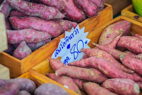 Organic Japanese sweet potatoes for sale at the local fresh market with price tag. Roasted sweet potato is a popular winter street food in East Asia. Purple and yellow sweet potatoes on sale.