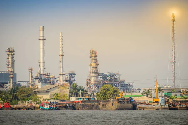 Oil refinery plant at riverfront of Chao Phraya river in Bangkok, Thailand. Heavy industrial oil refinery riverfront with daylight and blue sky background.