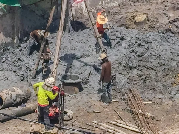 Bored piling workers are drilling mud hole with tripod rig and steel cages in the construction site and the reinforcement bar will be dropped into place and concrete will be poured into the bore hole.