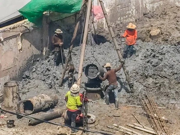 Bored piling workers are drilling mud hole with tripod rig and steel cages in the construction site and the reinforcement bar will be dropped into place and concrete will be poured into the bore hole.