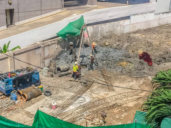 Bored piling workers are drilling mud hole with tripod rig and steel cages in the construction site and the reinforcement bar will be dropped into place and concrete will be poured into the bore hole.