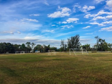 Kale direği ve mavi gökyüzü ve bulutlar beyaz arka plan ile kırsal alanda yerel futbol stadyumu. Yeşil çimen, kale direği ve mavi gökyüzü arka plan ile il okulda futbol sahası.