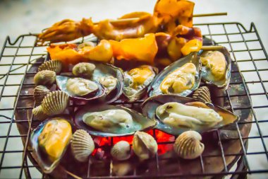 Mürekkep, midye ve istiridye üzerinde gece partide soba kömür ızgara. Deniz ürünleri Barbekü partisi ile kalamar calamaris, midye ve istiridyeler ateşe ızgara. Barbekü kavramı, seçici odak.