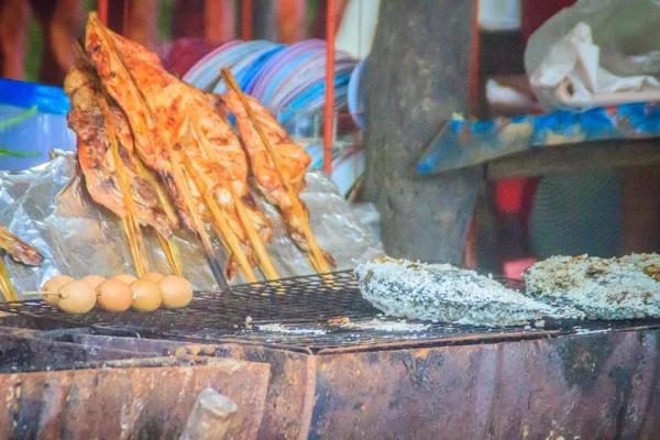 Salt coated tilapia fish that grilled on charcoal stove. Grilled chicken in bamboo stick and grilled eggs for sale. Street food stall vendor is grilling for tilapia fish, eggs and chickens.