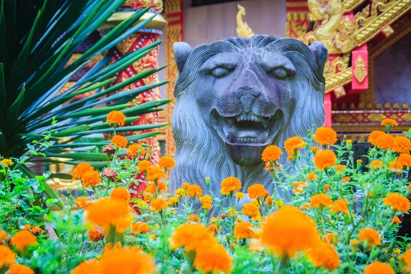 Lion statue at the entrance to the temple with yellow marigold flowers on tree foreground decoration.