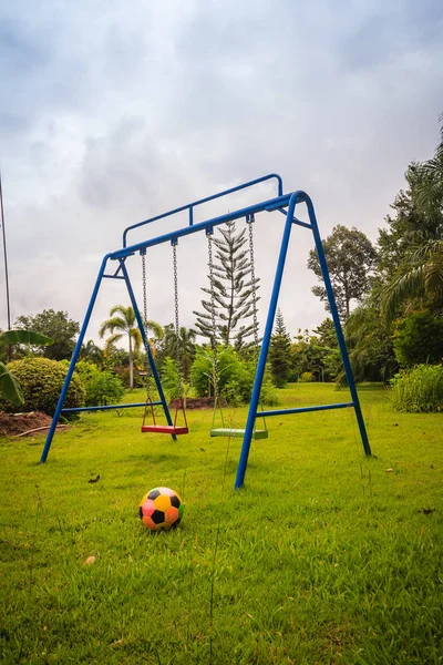 Playground equipment in the backyard for kids with soccer goal net and football on green grass field background.