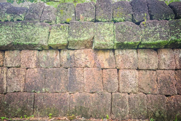 Laterite stone wall with grass and moss growth forming beautiful textured on the surface for background. Old laterite bricks texture with green grass and fresh moss.